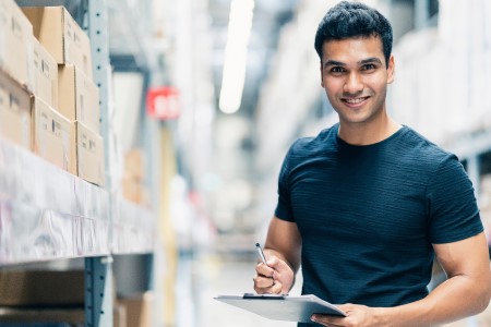 Man smiling while holding a clipboard in a warehouse