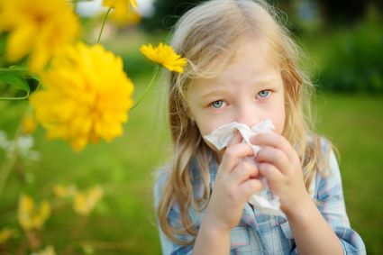 Girl blowing her nose outdoors next to flowers