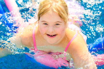 Smiling young girl in a pink swimsuit swimming in a pool on a sunny day.
