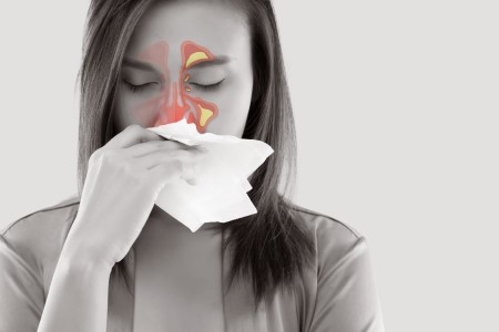 A woman blows her nose; an illustration over the photo shows the location of her sinuses