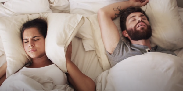 A frustrated woman lies in bed next to her snoring partner