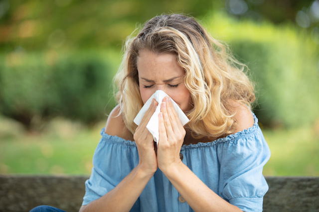 Woman sneezing into tissue due to summer allergies