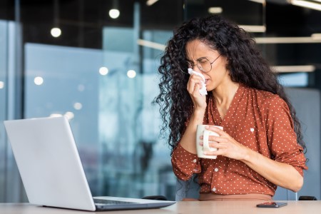 Women sneezing while sitting in front of a laptop in an office